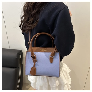 Detail of light purple pebbled leather handbag with dark brown flap and gold lettering