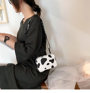 Side view of a mini suitcase crossbody bag with trendy black and white cow print