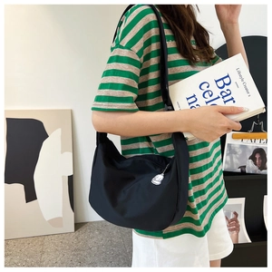 Detail of black nylon crescent crossbody bag with white charm on striped outfit