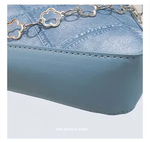 Detail showing precise stitching and plum blossom shaped metal chain buckle on blue handbag