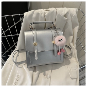 Détails d'un mini sac à dos argenté avec boucles dorées et breloque en peluche rose