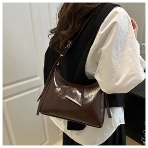 Close-up of a brown patent leather Hobo bag with silver metal bar detailing on shoulder