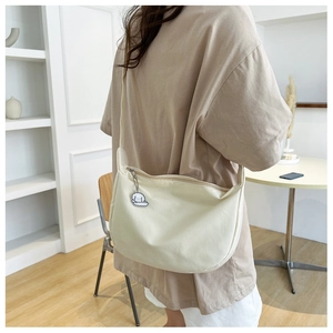 Detail view of cream canvas crescent bag with cute fluffy dog charm and zipper closure