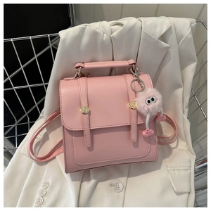 Détail d'un mini sac à dos rose clair avec boucles dorées et pompon sur un blazer blanc