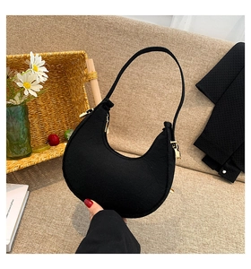 Detail of a black felt crescent bag with gold zipper held against a cozy home background