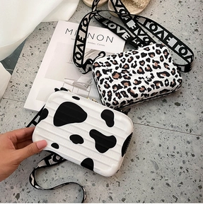 Close-up of mini hard shell bags with leopard and cow prints on a gray textured floor