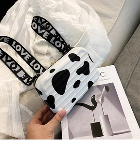 Detailed macro shot of the cow print mini suitcase crossbody bag and wide love strap