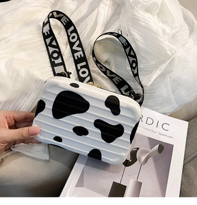 Detail of cow print suitcase-shaped mini bag with LOVE jacquard strap on a Nordic magazine