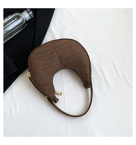 Macro detail of dark brown crocodile embossed texture and gold zipper on a crescent bag
