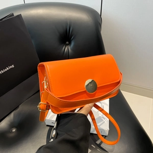 Sac baguette en cuir orange avec boucle dorée circulaire sur un fond noir élégant
