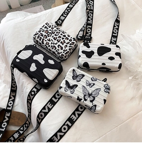 Detail of mini suitcase crossbody bags with butterfly, leopard, and cow prints on a bed