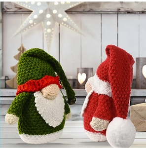 Close-up of two handmade knitted Christmas gnomes on wooden table with warm fairy lights