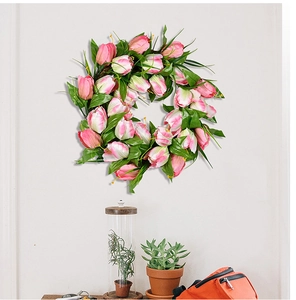 Detail of pink tulip wreath with green leaves on white wall for home door decor