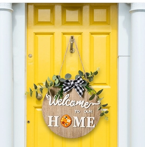 Detail of round wooden door sign with 3D Welcome text and green plant bow on yellow door