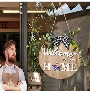 Close-up of wooden Welcome To Our Home sign with USA flag star and greenery on glass door