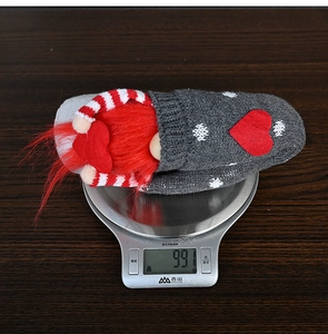 Close-up of knitted faceless gnome toy with red heart detail on a digital scale