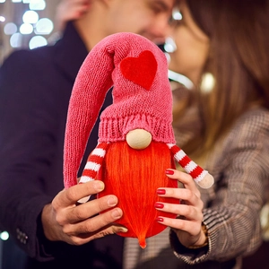 Knitted Valentine Gnome doll with red heart hat and long plush beard on festive background