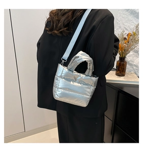 Bolso cubo acolchado plateado con correa extraíble mostrado por una modelo en interior