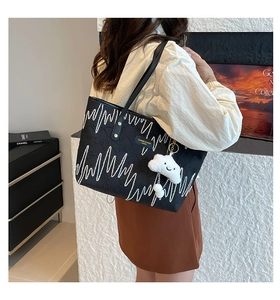 Detail of black tote bag with white wave embroidery and cute cloud plush charm accessory