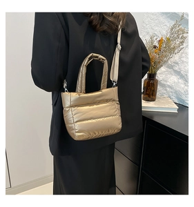 Detalle de bolso cubo acolchado dorado con asa y correa ajustable mostrado en un modelo