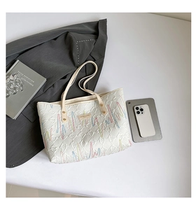 Detail of a large cream quilted tote bag with colorful embroidery and long shoulder straps