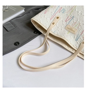Close-up of cream quilted tote bag featuring wave embroidery and metal logo on blazer