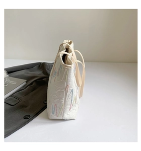 Detail of white quilted tote bag with colorful wavy stitching and slim leather shoulder strap