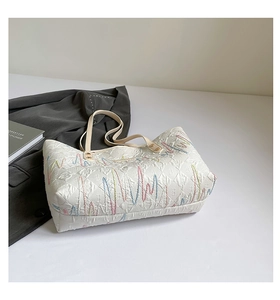 Detailed close-up of white nylon tote bag with colorful embroidery and leather straps