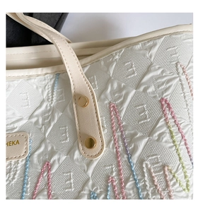 Detail of quilted white tote bag featuring colorful embroidery and gold rivet leather handle