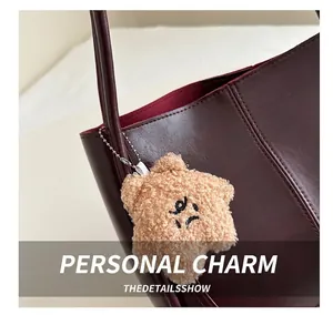 Detail of star-shaped plush pendant with embroidered face on burgundy leather shoulder bag
