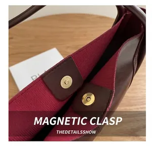 Close-up of golden magnetic hardware buckles and red fabric lining of the tote bag