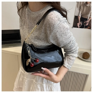 Détail du sac sous le bras en cuir verni noir avec chaîne et accessoire de breloque cerise