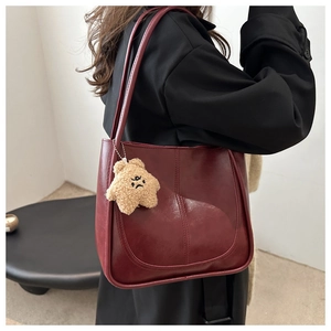 Detail of burgundy vintage tote bag with curved stitching and a cute bear charm