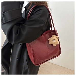Detail of dark red tote bag with plush charm on black coat, showcasing the leather texture