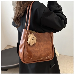Detail of vintage brown textured tote bag with U-shaped stitching and teddy bear charm