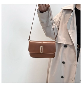 Nahaufnahme einer braunen Leder-Baguette-Tasche mit Goldverschluss am beigen Trenchcoat