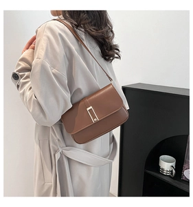 Detail einer braunen Lederschultertasche mit Metallschnalle auf einem beigen Mantel