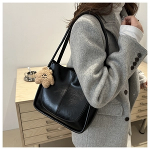 Detail of black faux leather tote bag with a brown plush bear charm and sleek stitching