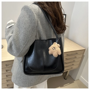 Detail of black faux leather tote bag with plush star charm on a casual grey blazer