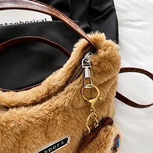 Primer plano de un bolso de peluche marrón con cremallera plateada y un tierno amuleto de oso
