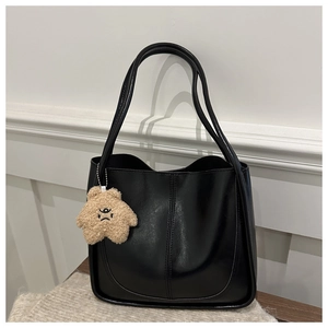 Detail of minimalist black tote bag featuring vertical seams and a cute brown plush bear charm
