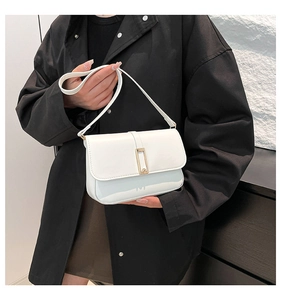 Detailansicht der weißen Leder-Schultertasche mit Goldschnalle auf schwarzem Mantel