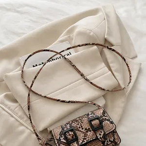 Détail d'un petit sac carré imprimé serpent avec rabat posé sur une veste chic
