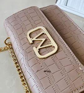 Primer plano de bolso en piel con grabado de cocodrilo, gran logo dorado y cadena