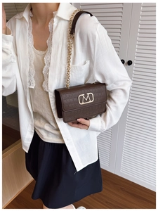 Bolso bandolera marrón de coco con hebilla M dorada y correa de cadena en una modelo