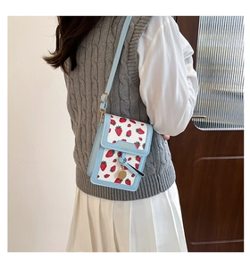 Detail of light blue crossbody bag with strawberry print and gold fashion logo