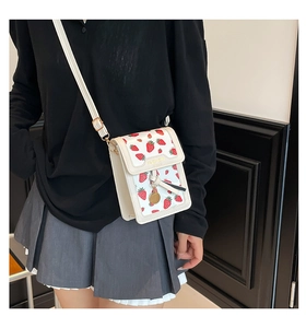Detail of white strawberry print crossbody bag with gold Fashion logo and metal pendant