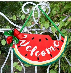 Wooden watermelon welcome sign with bow hanging on a white fence with green plants