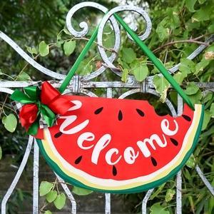 Watermelon welcome door sign with colorful bow hanging on a white decorative garden gate