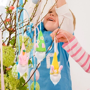Easter gnome plush pendants with bunny ears being hung on a spring tree by a child